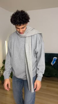 Grå oversized genser laget av mykt materiale, kombinert med et lyst grått ribbestrikket skjerf drapert rundt halsen. Blå jeans fullfører antrekket.