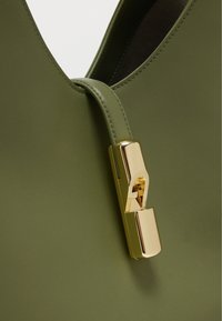 Πράσινη δερμάτινη τσάντα χειρός με έντονο κούμπωμα σε χρυσό τόνο με γεωμετρικό σχέδιο και στρογγυλεμένο λουρί ώμου. Ματ υφή με υφή.