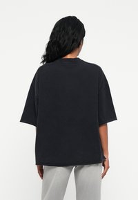 Μαύρη oversized μπλούζα, κοντά μανίκια, στρογγυλή λαιμόκοψη, φτιαγμένη από μαλακό βαμβακερό ύφασμα. Καθαρός, μίνιμαλ σχεδιασμός χωρίς ορατά σχέδια ή λεπτομέρειες.