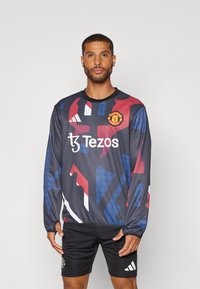 Maglietta sportiva a maniche lunghe di colore grigio scuro con motivi astratti blu, rossi e bianchi, caratterizzata da un colletto rotondo e dal logo del Manchester United.