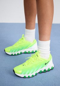 Neongröna sportskor med en texturerad ovandel, vit sula och runda gröna detaljer. Har snörning och en svart Nike-logotyp på sidan.