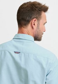 Camicia azzurro chiaro con bottoni realizzata in cotone, dotata di un colletto a punta e di una piccola etichetta a righe sul retro, vicino al colletto.