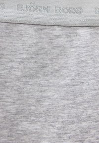 Ανοιχτό γκρι ύφασμα με ελαφρώς υφασμένη υφή και κοντινή εικόνα μιας μέσης με τη λέξη "BJÖRN BORG" σε ανάγλυφα γράμματα.