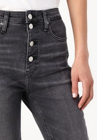 Svarta högmidjade jeans i jeansmaterial, med fem knappar fram, sydda fickor och en något texturerad yta.