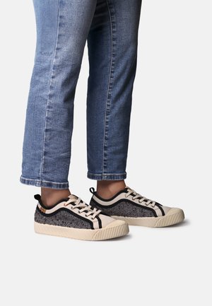 Sportbačiai su smėlio spalvos drobine priekiu, juodu ir pilku tekstūruotu paviršiumi, juodais akcentais ir kremine briaunota padais, dėvimi su mėlynais džinsais.