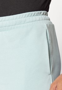 Calças de jogging azul claro com um tecido texturizado, apresentando uma cintura elástica e bolsos laterais. A vista em close destaca os detalhes do material.