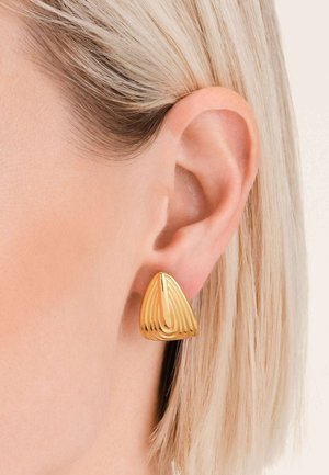 Zlatne trokutaste naušnice s valovitim, reljefnim dizajnom. Glatka tekstura i polirana obrada. Nosi se uz kratku frizuru blizu uha.