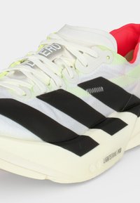 Scarpa sportiva bianca con strisce nere, lacci bianchi, fodera interna rossa e scritta "LIGHTSTRIKE PRO" sulla suola.