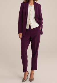 Purple tailored suit with structured jacket and tapered trousers, paired with a cream button-up cardigan and grey stiletto heels.