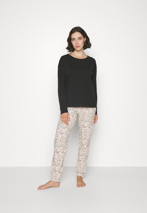 Svart långärmad topp kombinerad med mönstrade kräm- och rosa pyjamasbyxor med zigzag-mönster och elastiska anklar.