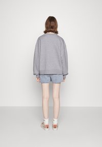 Šedá oversize mikina, džínové šortky a béžové tenisky s červenými akcenty. Jednoduché pozadí, pohodlný design a uvolněný střih.