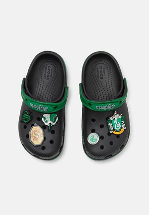 Black Crocs with a green strap, featuring Slytherin-themed decorative pins, showcasing a smooth texture and multiple ventilation holes.