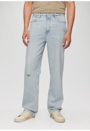 Lichtblauwe denim jeans met een ontspannen pasvorm, met een scheur op de linkerknie, eenvoudige stiksels en een metalen knoopsluiting. Gemaakt in combinatie met beige sneakers.