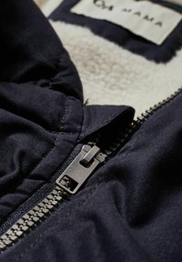 Primer plano de una chaqueta negra parcialmente cerrada que muestra los dientes de la cremallera de metal y el suave forro de felpa blanca en su interior.