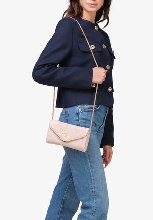 Borsa a tracolla in suede rosa con una tracolla in oro e un dettaglio con il logo. Presenta una patta pieghevole e una texture morbida.