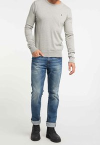 Grauer Pullover, Rundhalsausschnitt, körperbetont mit gerippten Bündchen, kombiniert mit blauen Jeans mit umgeschlagenen Säumen und schwarzen Schnürstiefeln.