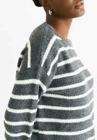 Gray sweater featuring horizontal white stripes, a textured knit pattern, crew neckline, and long sleeves. Soft and casual design.