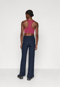 Dopasowany bordowy stanik sportowy z plecami w stylu racerback, zestawiony z granatowymi, prążkowanymi spódnicami z szeroką nogawką. Materiał wydaje się elastyczny i strukturalny.