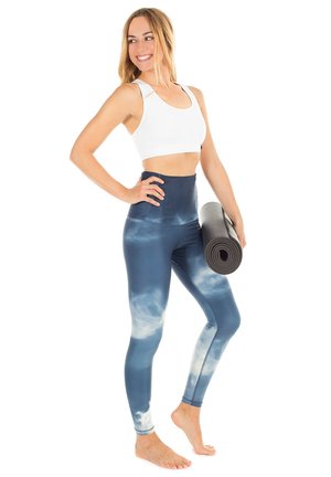 Högmidjade, blåa tie-dye leggings med en slät textur och stretchigt tyg, i kombination med en vit sport-bh och en rullad yogamatta.