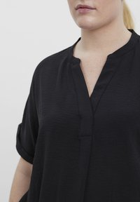 Zwarte blouse met korte mouwen, een notch-kraag, textuurstof en een losse pasvorm, voorzien van een voorste sluiting en omgeslagen mouwen.