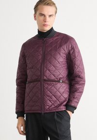 Quilted purple jacket with a zip front, featuring a high collar, side snaps, and black trim. Smooth texture with a diamond pattern design.
