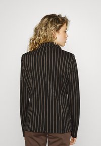 Black blazer with vertical stripes in brown. Tailored fit with a notched collar and structured shoulders. Smooth fabric, minimal detailing.