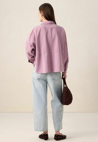 Oversized lavender jacket with a collar, light blue high-waisted jeans, and a brown studded handbag. Smooth fabric and relaxed fit.