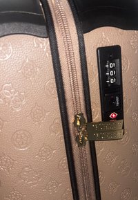 Maleta rígida en beige con un patrón floral en relieve, ribete negro, cerradura de combinación aprobada por la TSA y detalles en dorado.