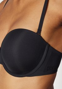 Sostén negro acolchado con copas moldeadas, correas ajustables y una textura suave. Presenta el logo de DKNY en el lateral y bordes sin costura.