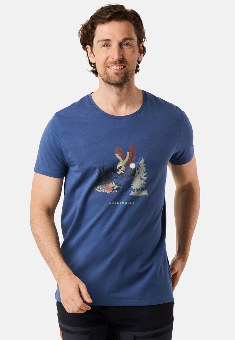 Blå bomullströja med korta ärmar och rund halsringning. Har en grafisk tryck av en örn och träd i jordnära färger.