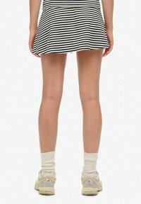 Gonna a righe bianche e nere con un design svasato. Abbinata a sneaker beige e calzini bianchi. L'attenzione è rivolta alla vista posteriore dell'outfit.