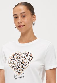 Weißes Baumwoll-T-Shirt mit einem großen Grafikmotiv eines goldumrandeten Herzens, das von mehrfarbigen Herzen umgeben ist, und dem Text "Liebe versagt nie" darunter.