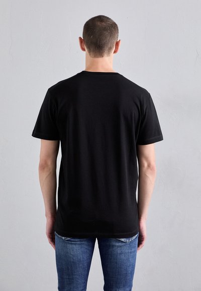 T-shirt in cotone nero con collarino rotondo, maniche corte e un design semplice, abbinato a jeans di denim blu. Mostrato da dietro.