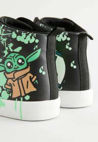 Schwarze High-Top-Sneaker mit grünem und braunem Grafikmotiv eines Charakters, weißen Gummisohlen und strukturierten schwarzen Stoffseiten.