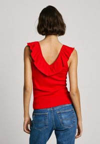Top rosso senza maniche con scollo a V e dettagli arricciati, abbinato a jeans in denim blu con tasche posteriori e taglio classico.