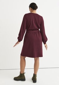 Bordowa sukienka z długimi bufkami, opinająca w talii. Gładki materiał, do kolan, noszona z ciemnozielonymi botkami. Prosty design.