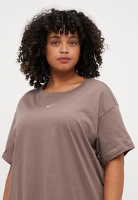 Ruda medvilnės marškinėliai su apvalia iškirpte ir trumpomis rankovėmis, puošti mažuoju baltu Nike logotipu ant krūtinės. Minkšta tekstūra, laisvas siluetas.