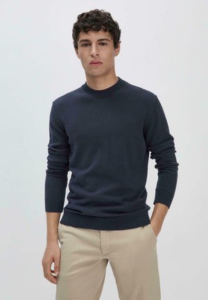 Marineblaues Rundhals-Sweatshirt aus weichem Strickstoff mit gerippten Bündchen und Saum, kombiniert mit beigen Hosen für einen monochromen Look.