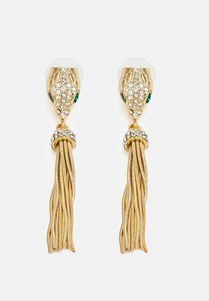 Kolczyki z głową węża w złotym odcieniu, z zielonymi oczami, kryształowymi detalami i wieloma delikatnymi łańcuszkami z frędzlami zwisającymi poniżej.