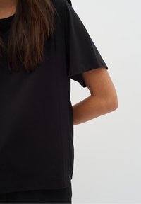 Svart t-shirt med kort ärm och avslappnad passform, tillverkad av mjukt tyg. Har en rund halsringning och subtil sömnad längs sidorna.