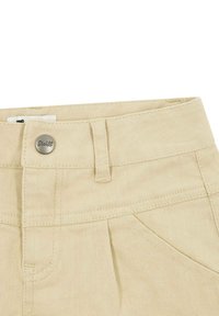 Los pantalones de algodón beige cuentan con una cinturilla plana, bolsillos frontales y un botón metálico con detalle de logo, exhibiendo costuras duraderas y una textura suave.