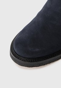 Embout de botte en velours bleu foncé avec semelle en caoutchouc noir cousue sur fond blanc.