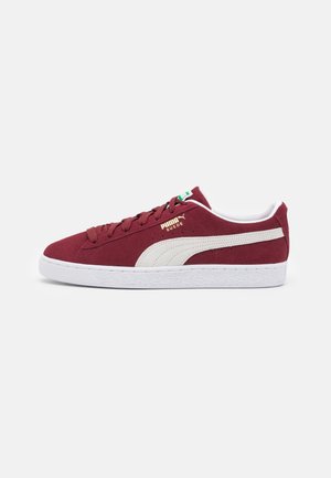 Sneaker rossa in suede con dettagli in pelle bianca, suola piatta in gomma bianca, punta arrotondata e finitura testurizzata. Presenta un logo dorato sul lato.