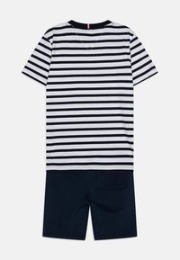Un T-shirt rayé avec des rayures horizontales bleu marine et blanches, associé à un short bleu marine. Le tissu semble lisse et comprend une poche sur le short.