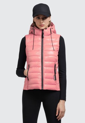 Rosa Puffer-Weste mit Kapuze, ausgestattet mit einem Frontreißverschluss, zwei seitlichen Taschen und schwarzen Zugbändern. Trägt man über einem schwarzen Langarmoberteil.