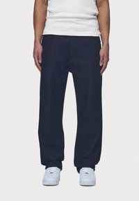 Dark blue denim pants with a relaxed fit, featuring front pockets and a waistband. Worn with white sneakers and a plain white t-shirt.