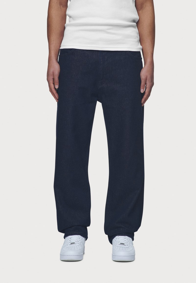 Dark blue denim pants with a relaxed fit, featuring front pockets and a waistband. Worn with white sneakers and a plain white t-shirt.