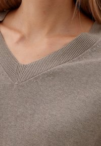 Pull en V dans un tissu beige doux, avec des détails côtelés le long de l'encolure et de subtils accents de couture.