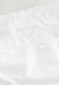 Mutande di cotone bianco con rifiniture in pizzo e piccoli fiocchi, disposte in un'armonia piegata, che mettono in evidenza una texture liscia e dettagli delicati.
