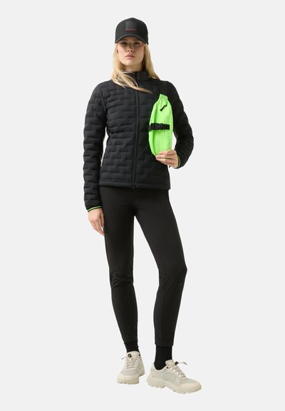 Polstret sort jakke med lynlås, parret med sorte leggings og lyse sko. Holder en lys grøn skuldertaske.
